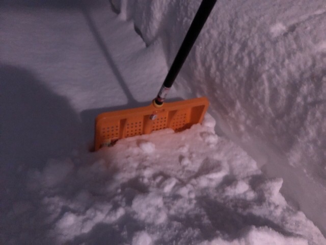 オレンジのスコップを玄関席に積もった雪に指し積雪量を測る