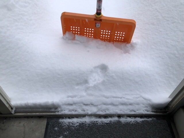 家の玄関を開けて雪かきのスコップを積もった雪にさす