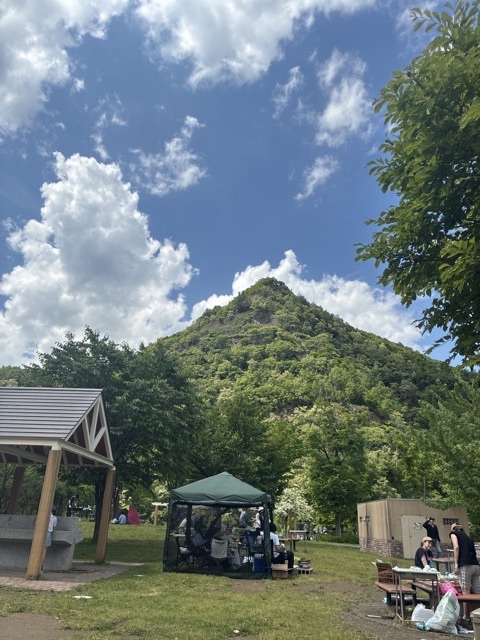 天山公園の砕石跡が伺える山をパックにテーキャンプのタープ
